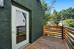 A wooden deck with a metal gate, a white door with a window, and a brick wall.