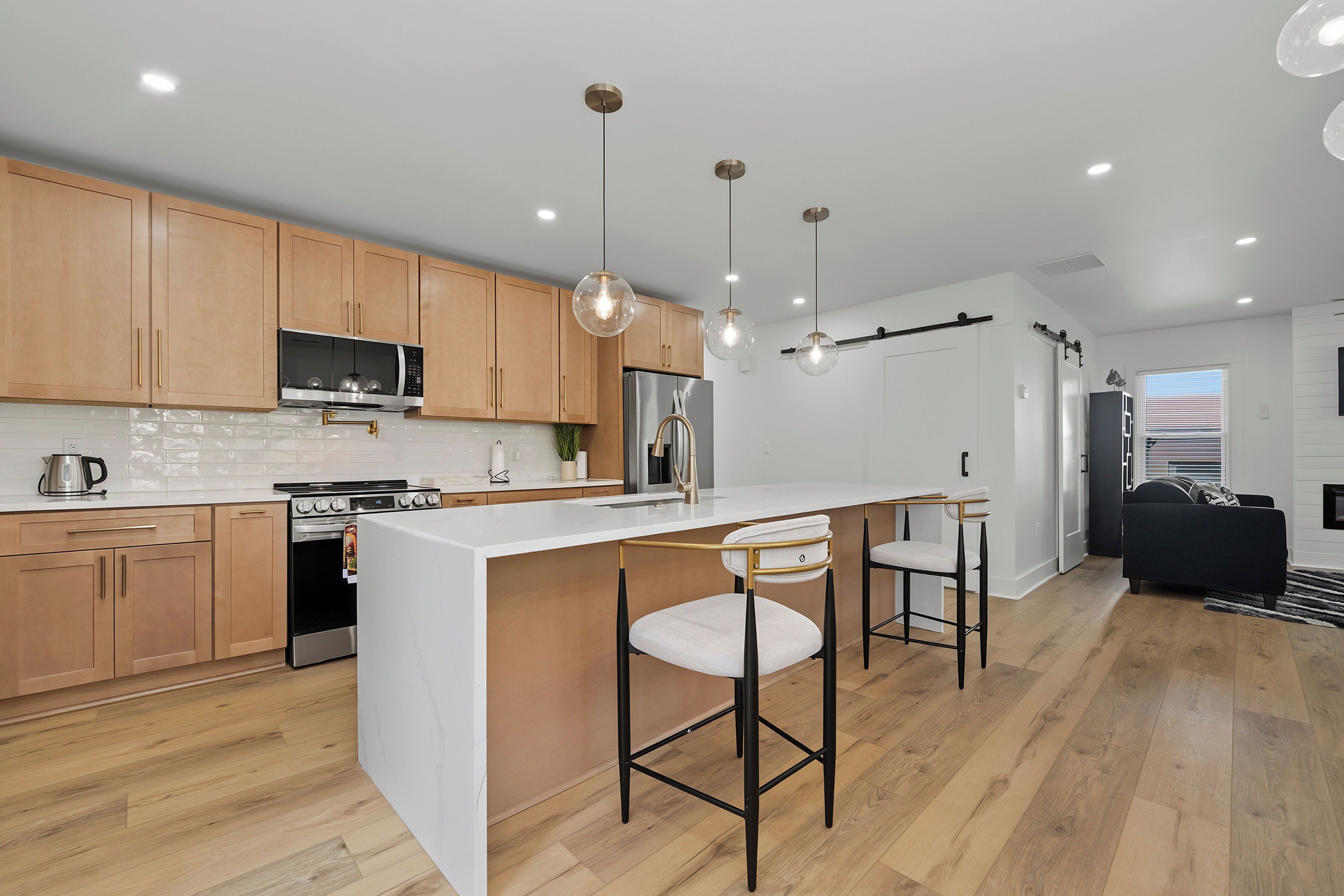 Une cuisine moderne avec des meubles en bois, des appareils électroménagers en acier inoxydable et des luminaires suspendus.