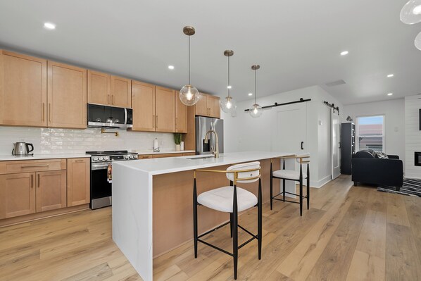 A modern kitchen with wooden cabinets, stainless steel appliances, and pendant lighting.