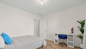 A bedroom with a bed, a desk, a chair, and a potted plant.