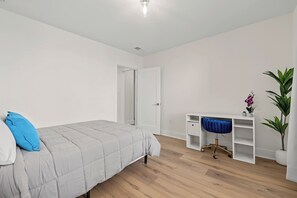 A bedroom with a bed, a desk, a chair, and a potted plant.