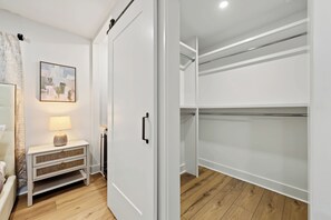 A modern interior with a walk-in closet, a bedside table with a lamp, and a wall-mounted abstract painting.