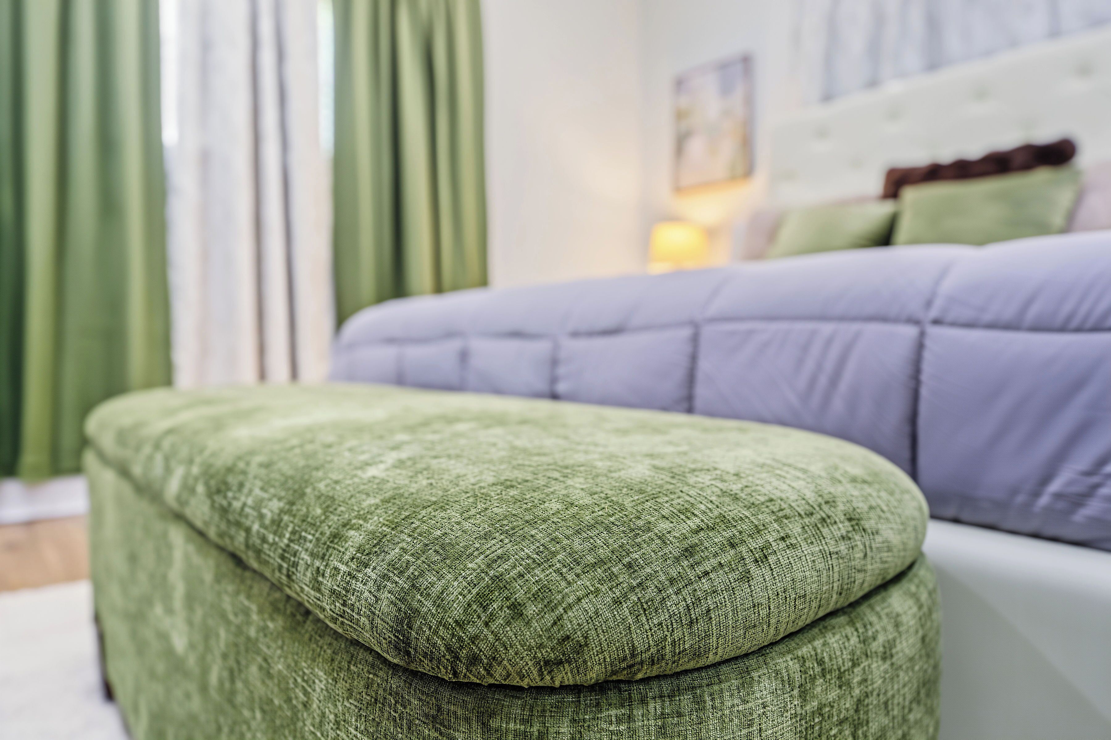 A room with a green upholstered bench, a purple sofa, and a bed with green pillows.