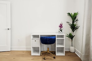 Un bureau blanc avec une chaise bleue, une plante en pot et une orchidée violette.