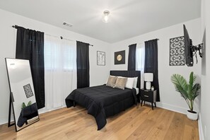 A bedroom with a bed, bedside tables, a lamp, a potted plant, and artwork on the walls.