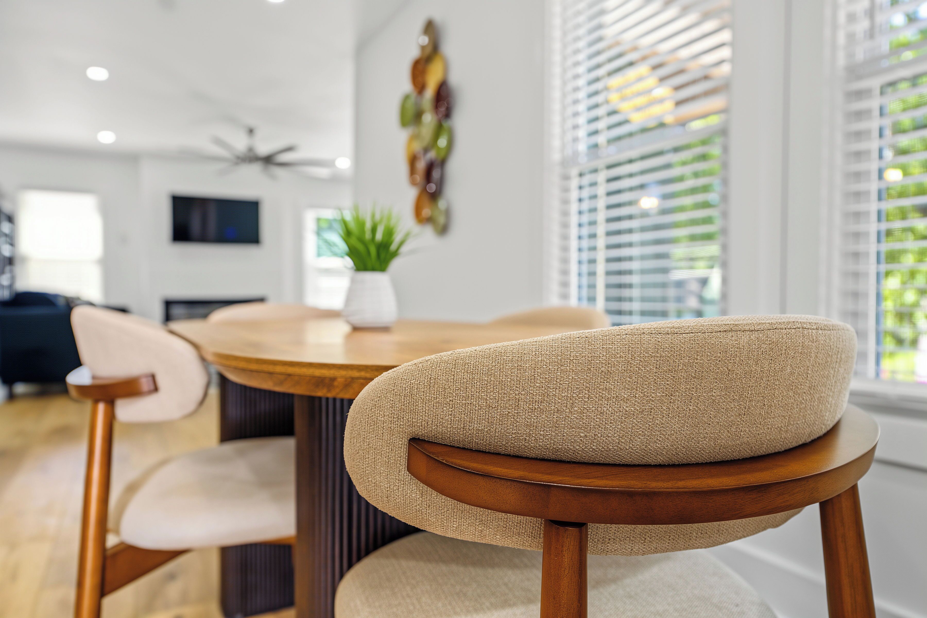 A dining area with a round table, two chairs with cushioned backs, a potted plant, and a ceiling fan.