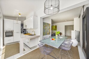 A modern kitchen with white cabinetry, a built-in oven, and a glass dining table with chairs. - Villa Casa Rafael by Villa Plus (Albufeira)