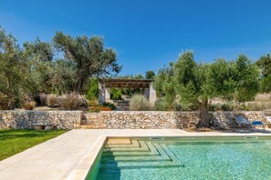 A swimming pool with a stone wall and a pergola in a landscaped garden. - Villa Simeone by Villa Plus (Ostuni)