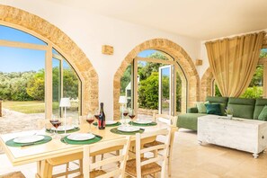 A dining area with a table set for two, a bottle of wine, and glasses. There are three arched windows providing a view of the outdoors. - Villa Simeone by Villa Plus (Ostuni)