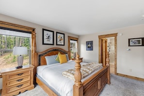 A bedroom with a large bed, a nightstand, a dresser, and a window with a view of trees. - Scenic and Spacious 4 Bedroom, 3.5 Bath Just Outside of Breckenridge (Blue River)