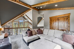 Ein modernes Wohnzimmer mit einem Ecksofa, Holzboden und einem großen Fenster mit Bergblick.