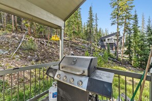 Ein Grill auf einem Balkon mit Blick auf eine bewaldete Landschaft und ein Haus im Hintergrund.