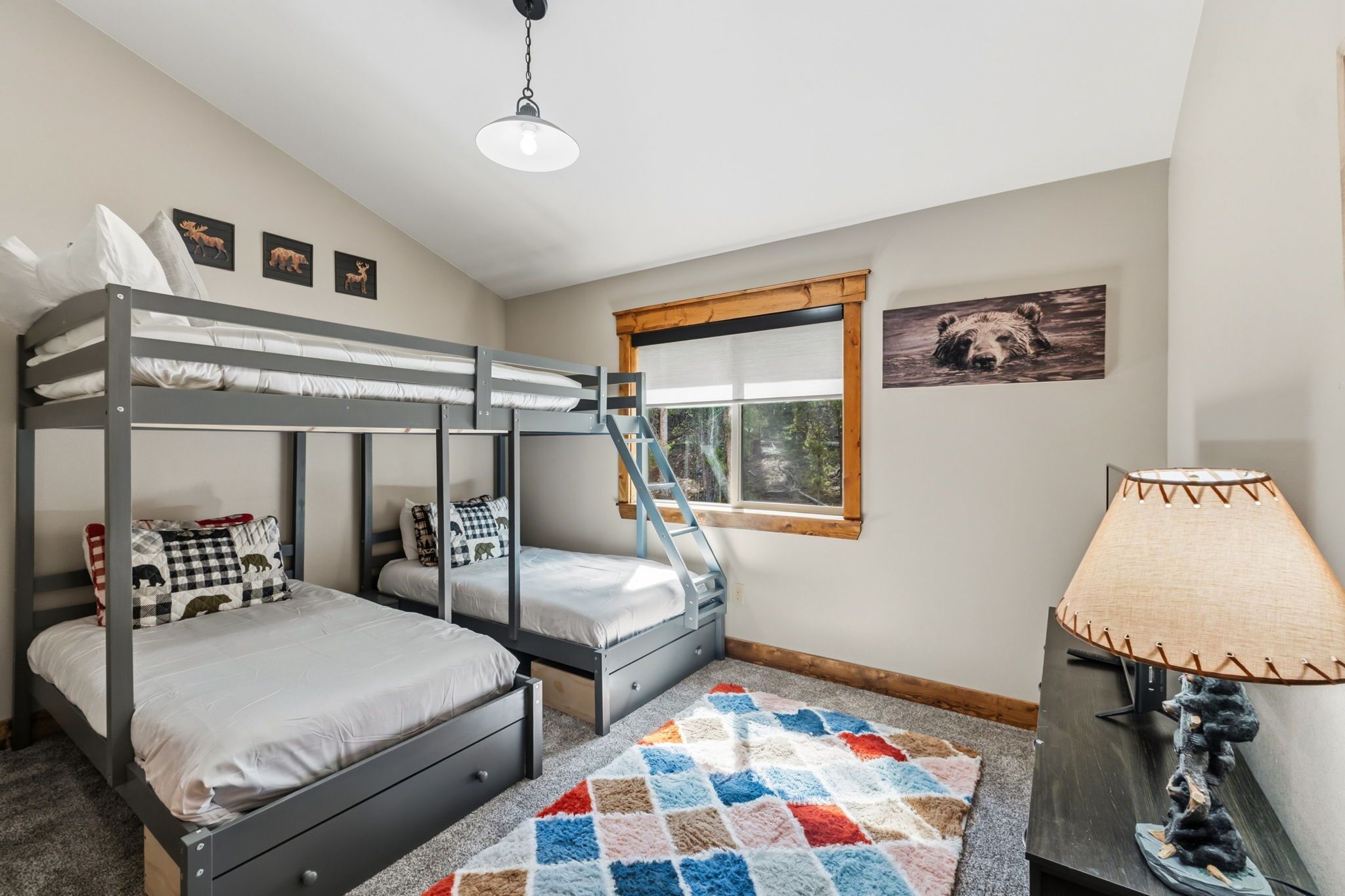 A bunk bed room with a window, a lamp, and a bear picture on the wall.