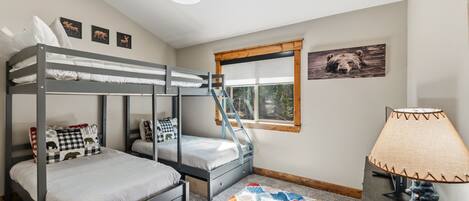 A bunk bed room with a window, a lamp, and a bear picture on the wall.