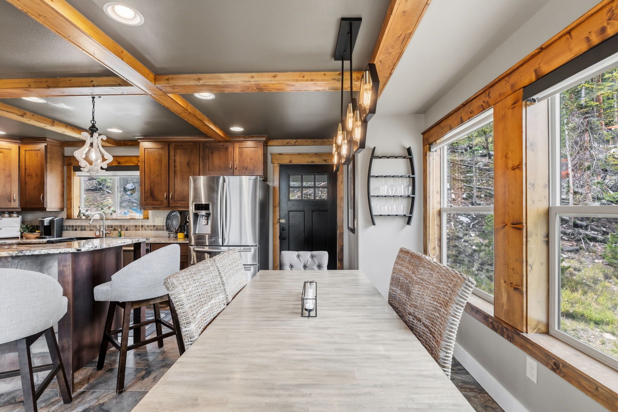 A modern kitchen with wooden beams, a central island, bar stools, and a dining table with a candle centerpiece.