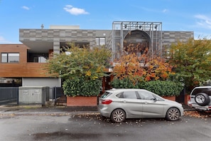 Ein modernes Gebäude mit Garagentor, einem davor geparkten Auto und einem Baum mit Herbstlaub.