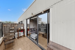 Eine moderne Wohnung mit Schiebeglastür zum Balkon, einem grauen Sofa und einem kleinen Tisch mit Lampe.