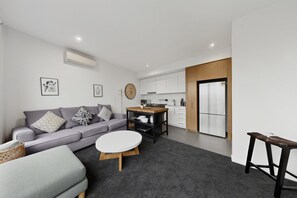 Ein modernes Apartment mit grauem Sofa, einem kleinen runden Tisch, einer Küchenzeile und einem Esstisch.