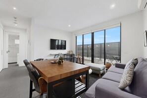 Ein modernes Wohnzimmer mit einem Holzesstisch, schwarzen Stühlen, einem grauen Sofa und einem großen Fenster mit Jalousien.