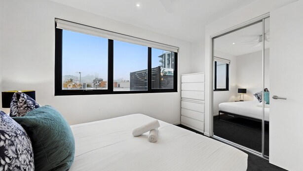 Un dormitorio moderno con un ventanal grande, una cama, una mesita de noche y un espejo.