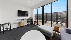 Una sala de estar moderna con un televisor de pantalla plana, un sofá, una mesita y un balcón con vista a la ciudad.