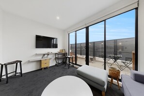 Ein modernes Wohnzimmer mit Flachbildfernseher, einer Couch, einem kleinen Tisch und einem Balkon mit Blick auf die Stadt.