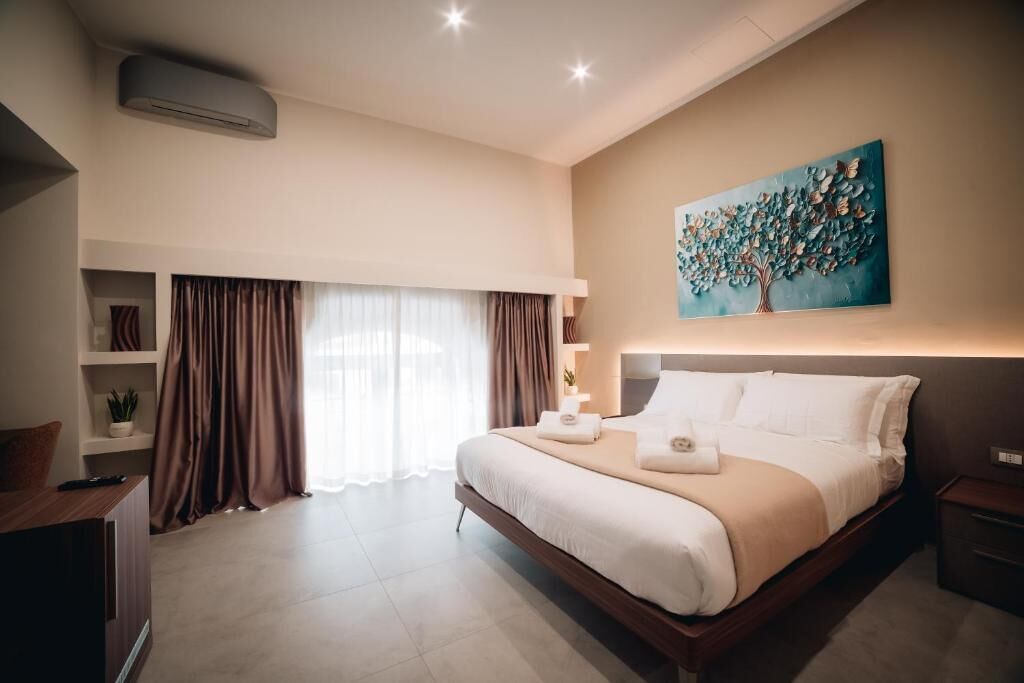 A hotel room with a large bed, a painting on the wall, and a window with curtains.