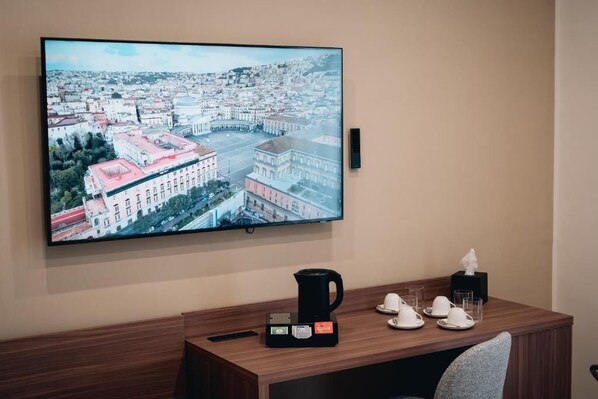 Une chambre d’hôtel dotée d’un grand téléviseur fixé au mur, qui diffuse des images d’un paysage urbain, d’un bureau en bois avec une machine à café et d’une chaise.