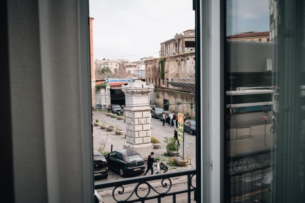 A view from a window overlooking a street with parked cars, a pedestrian, and buildings.