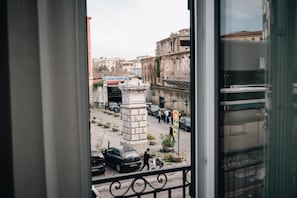 Uitzicht vanuit een raam op een straat met geparkeerde auto's, een voetganger en gebouwen.