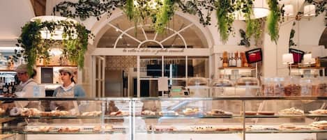 A bakery display case with various baked goods, a staff member behind the counter, and hanging greenery above.