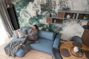 A modern living room with a blue sofa, a round wooden coffee table, and a decorative shelf with vases. - Apartment with a roof terrace - Seaside (Gdańsk)