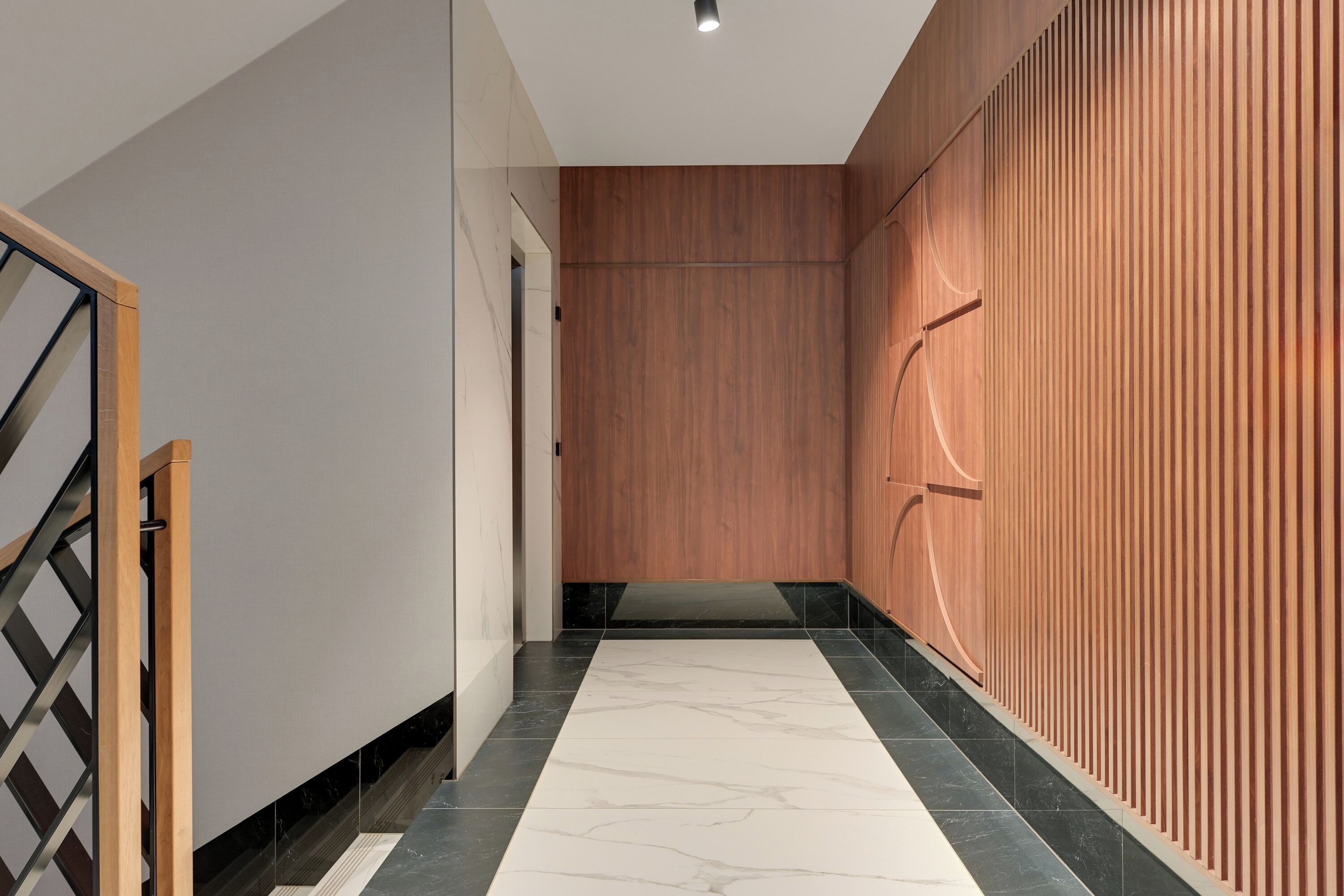 Un couloir moderne avec un mur lambrissé en bois, un sol en marbre et un escalier en métal.