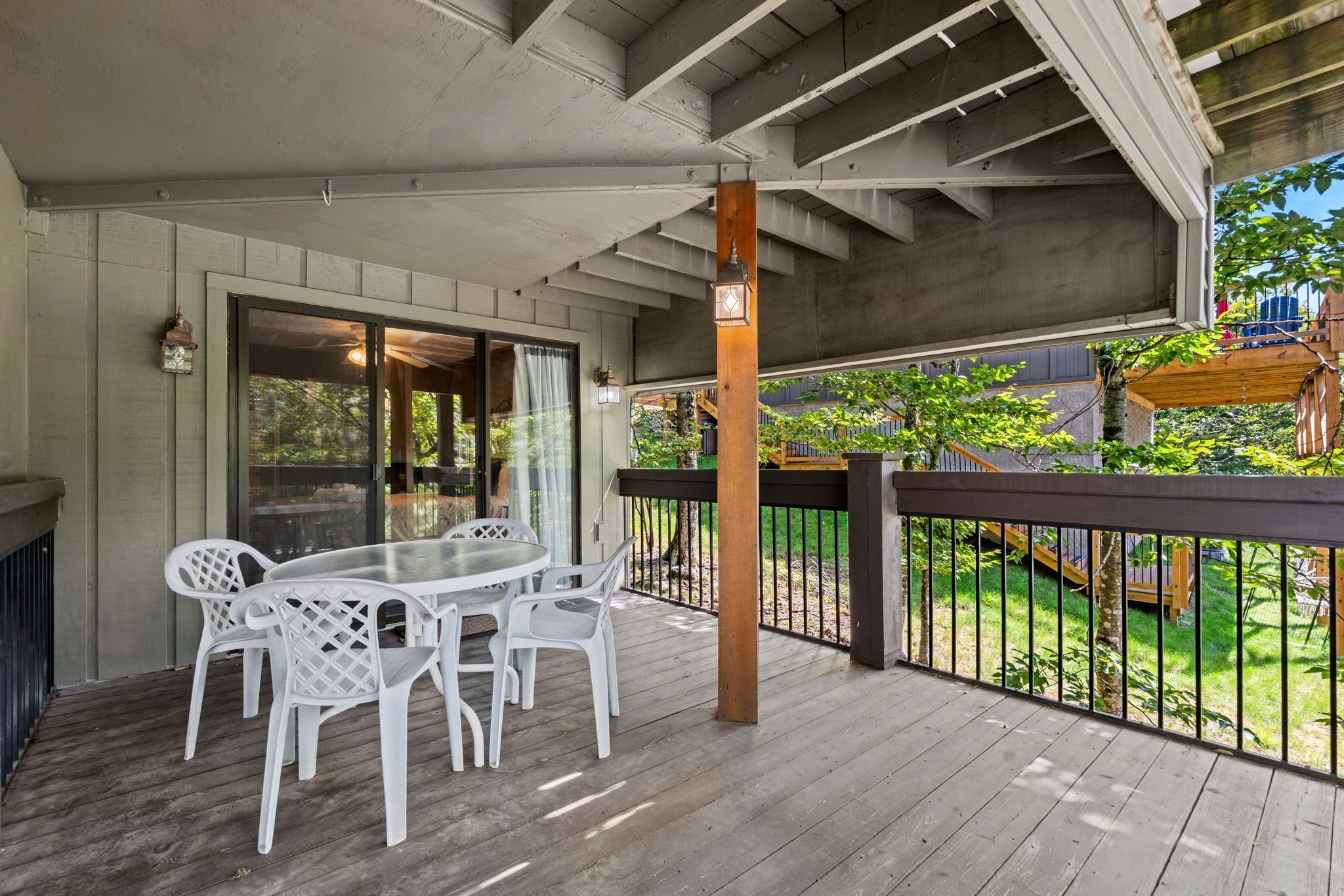A covered outdoor patio with a table and chairs, a wooden railing, and a view of a backyard.