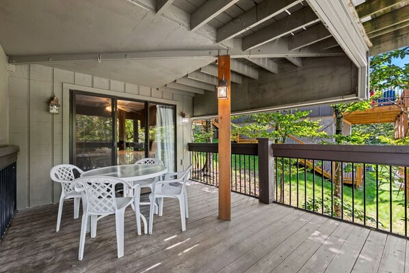 A covered outdoor patio with a table and chairs, a wooden railing, and a view of a backyard.
