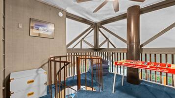 Une pièce avec un ventilateur de plafond, un tableau encadré, une commode blanche, un tapis bleu et une table de baby-foot.