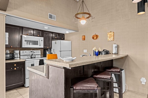A modern kitchen with dark wood cabinets, stainless steel appliances, a bar area with stools, and decorative wall art.