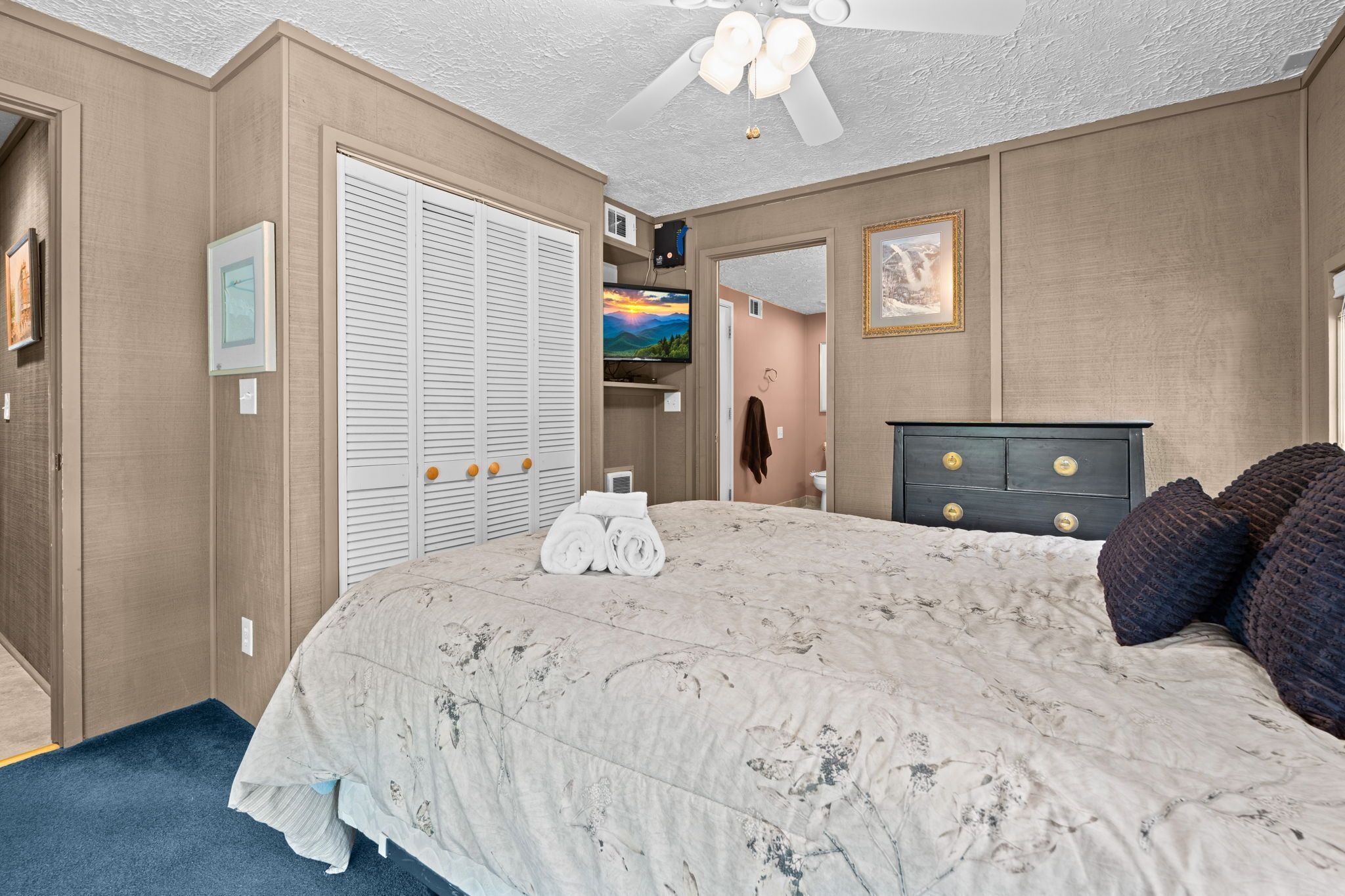 A bedroom with a bed, a wardrobe, a television, and a ceiling fan.