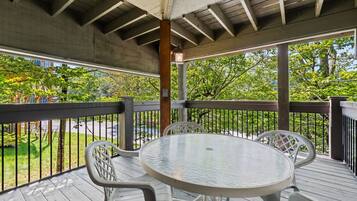 Un espace extérieur abrité, doté d’une table ronde et de chaises, entouré d’une terrasse en bois et d’une rambarde en métal.