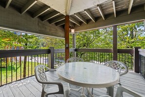 Een overdekt buitengebied met een ronde tafel en stoelen, omringd door een houten terras en een metalen hekwerk.