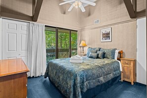 A bedroom with a bed, a nightstand, a lamp, a ceiling fan, and a window with curtains.