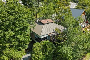 A house surrounded by dense trees with a visible deck and a sloped roof.