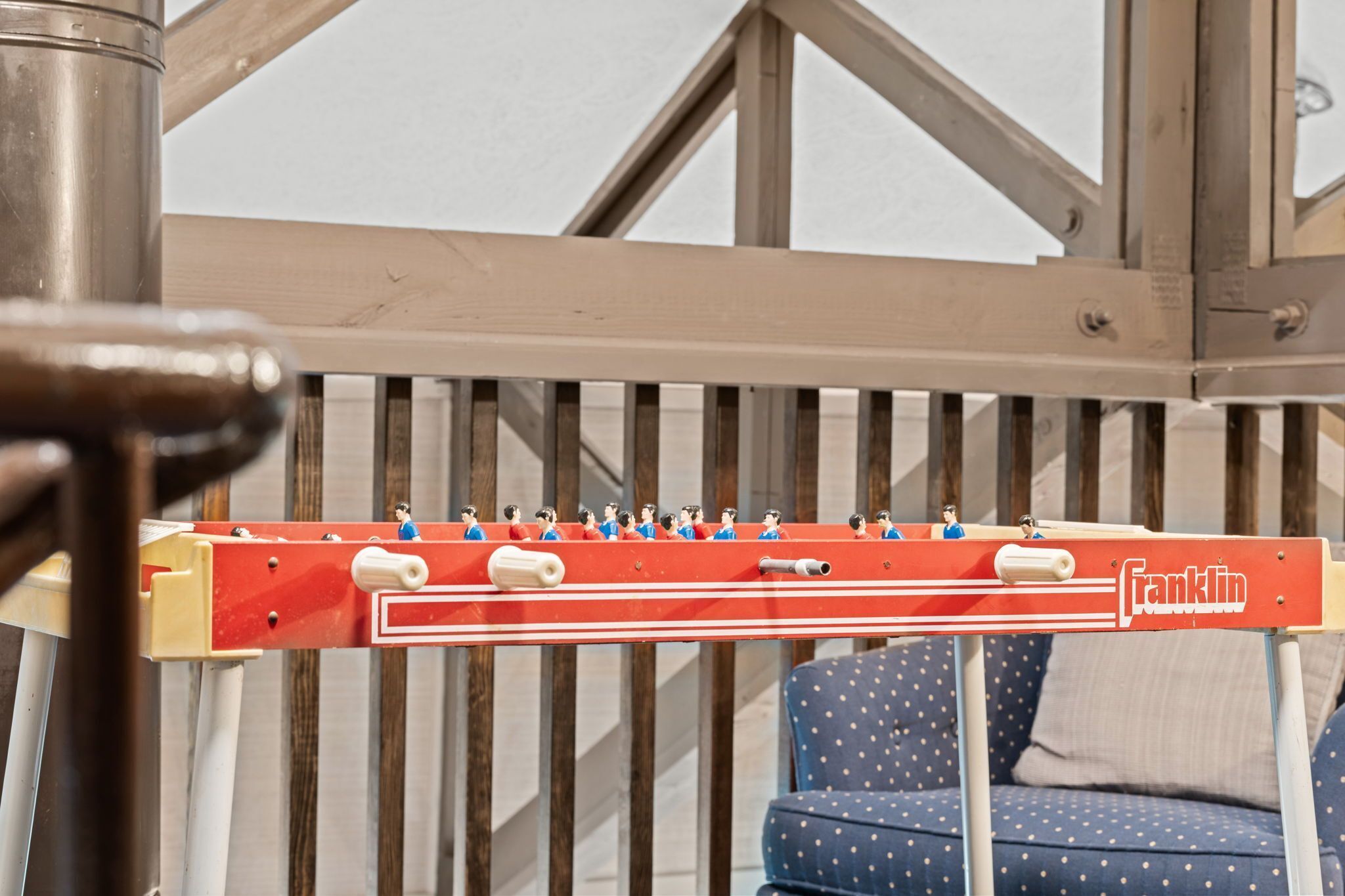 A red foosball table with the brand name 'Franklin' on it, set against a wooden structure with a blue polka-dotted sofa in the background.