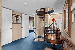 Un escalier en colimaçon avec des marches bleues et une table en bois surmontée d’une lampe en laiton.