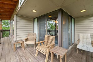 A wooden deck with a covered area, featuring a wooden chair, a small table, and a cushioned chair.