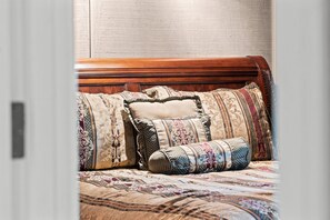 A view through an open doorway of an ornate wooden bed dressed in patterned pillows.