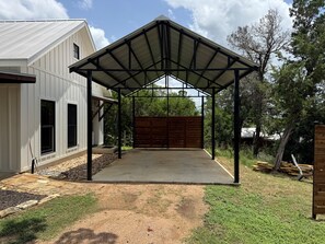 Ein überdachter Patio-Bereich mit Metall-Dach, Betonboden und einem Holzzaun im Hintergrund.