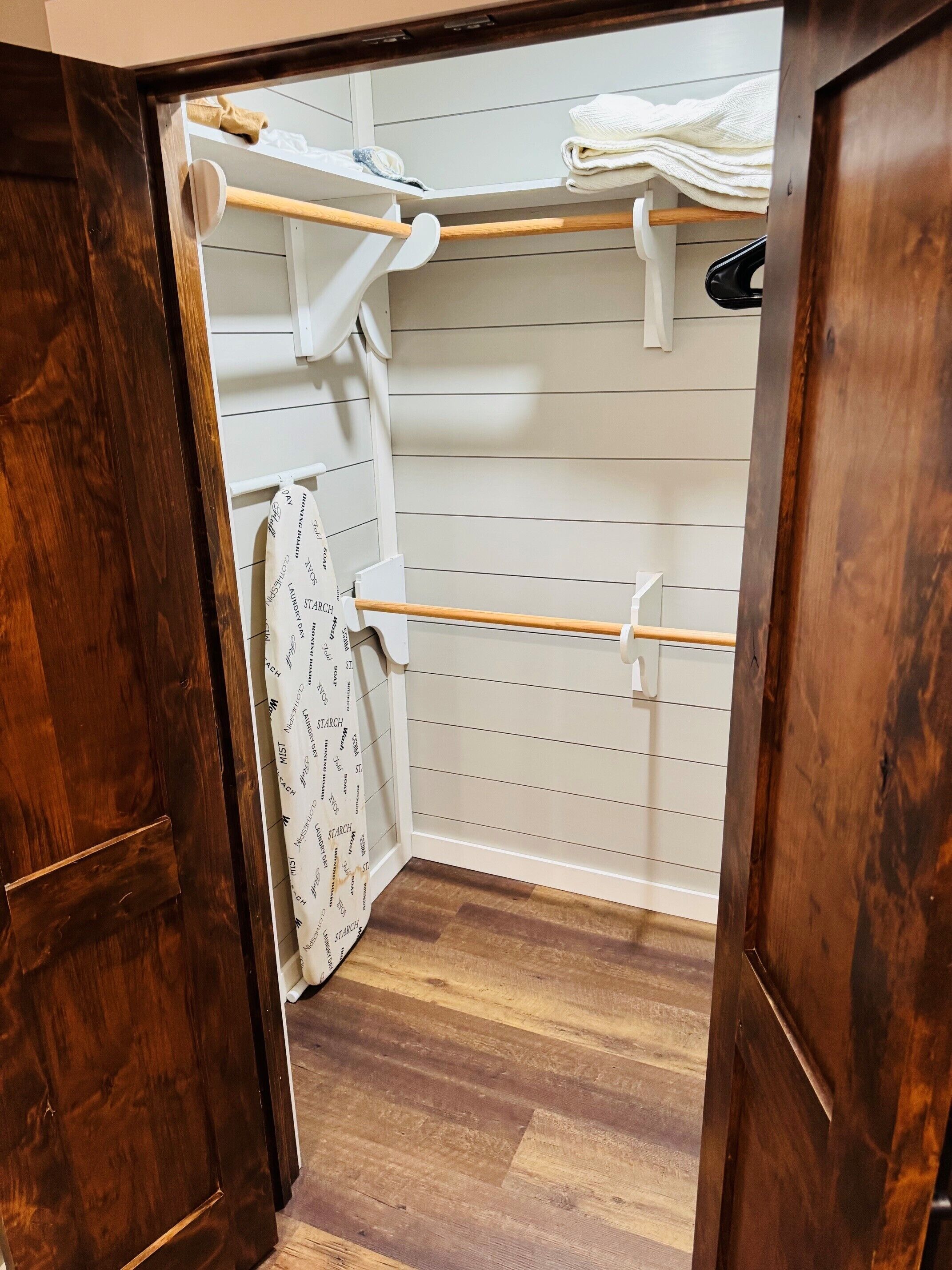 A wooden closet with hanging rods and a folded towel rack.