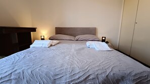 A neatly made bed with pillows and folded towels, two bedside lamps, and a wardrobe in a hotel room. - Private Room at the Villa nel Verde Residence in Rome-Ciampino (roma)