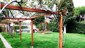 A garden with a wooden pergola, a swing set, and a paved walkway. - Private Room at the Villa nel Verde Residence in Rome-Ciampino (roma)